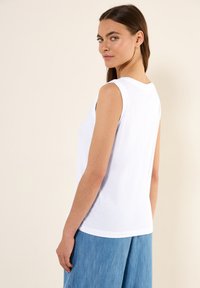 Top blanco sin mangas con cuello redondo, hecho de una suave mezcla de algodón. Presenta un corte relajado, complementado con pantalones de pierna ancha en azul claro.