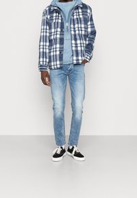 Rutig blå och vit flanellskjorta över en ljusblå jumper, kombinerat med ljusblå jeans och svart-vita sneakers. Avslappnad passform.