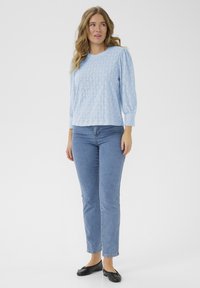 Lichtblauwe, getextureerde pullover met een ruitenpatroon, lange mouwen en een ronde hals, gecombineerd met strakke blauwe jeans en zwarte ballerina's.