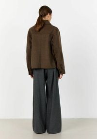 Brown wool blend jacket with a collar, long sleeves, and buttoned cuffs, paired with wide-leg gray trousers in textured fabric.