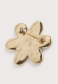 Broche en métal doré en forme de fleur avec un fermoir à épingle au dos pour la fixation sur les vêtements, présentée sur un fond clair.