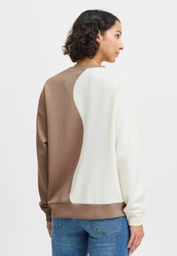 Sweatshirt coloré en marron et crème, à manches longues et col rond, avec une texture lisse et douce et une coupe décontractée.
