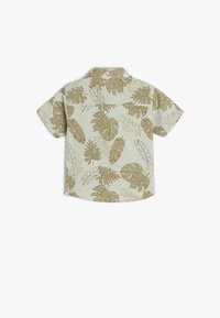 Beige shirt met korte mouwen en een tropisch bladpatroon in lichtbruin en groen, weergegeven vanuit de achterkant op een witte achtergrond.