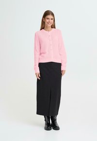 Rosa stickad cardigan med långa ärmar och rund halsringning, med knappstängning. I kombination med en svart maxikjol och svarta stövlar.