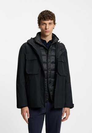 Veste noire imperméable avec plusieurs poches avant, capuche amovible et doublure matelassée. Tissu texturé et accents métalliques.
