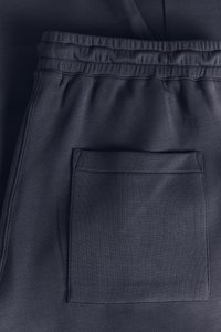 Ciemnoszare spodnie dresowe z teksturowanej tkaniny, z elastycznym pasem i dużą naszywaną kieszenią z tyłu.