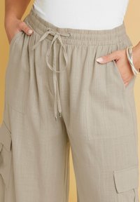 Beiga linne cargo byxor med dragsko i midjan, sidfickor och lapplommer på benen; textil med en lätt lyster.