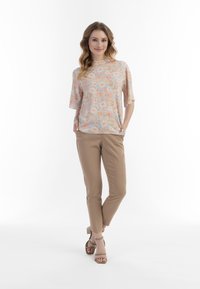 Top corto a maniche corte con motivo floreale in colori pastello, abbinato a pantaloni slim-fit beige e sandali con tacco marrone chiaro.
