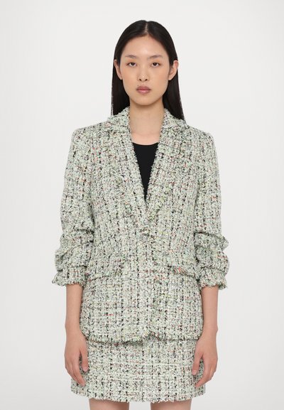 Blazer en tweed texturé vert et blanc avec des fils multicolores, revers crantés et manches légèrement retroussées, associé à une jupe assortie.