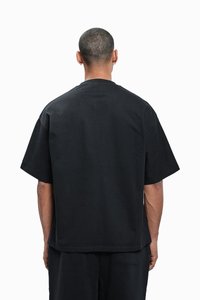 Černé oversize tričko s krátkým rukávem vyrobené z bavlny, s kulatým výstřihem a rovnou spodní částí, s hladkou matnou texturou.
