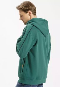 Zielona bluza z kapturem wykonana z miękkiego materiału, z kapturem na sznurki, bocznymi kieszeniami i kontrastującymi granatowymi paskami wzdłuż rękawów.