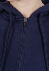 Felpa con zip di colore blu navy, dotata di cappuccio regolabile con cordino, caratterizzata da una texture liscia e una chiusura frontale con zip. Accentata da un tirazip nero.