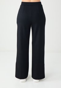 Pantalons larges noirs en tissu doux, avec une taille haute et des lignes épurées sans embellissements ni motifs visibles.