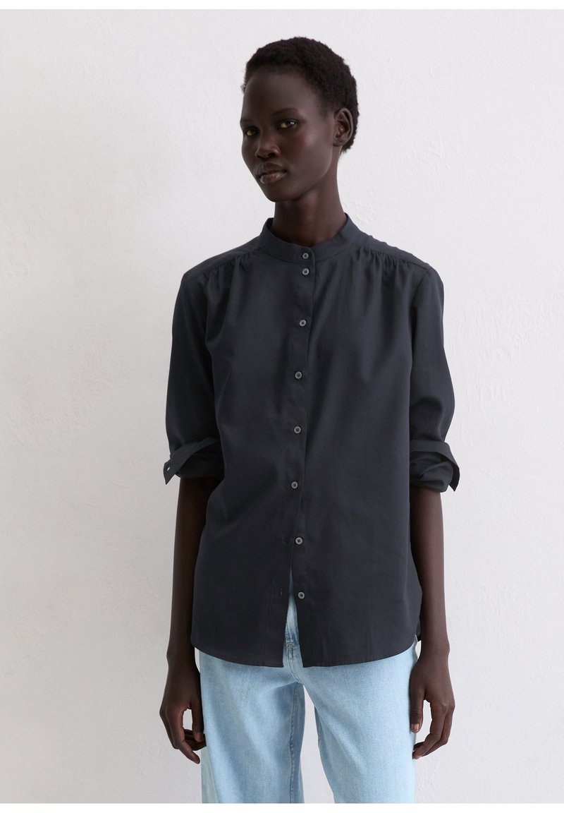 Czarna koszula na guziki z kołnierzykiem typu stójka, z podwijanymi rękawami i gładką fakturą, zestawiona z jasnoniebieskimi dżinsami.