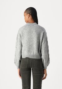 Gray knitted sweater with a ribbed hem, featuring puffed sleeves and a textured pattern. Paired with dark green corduroy pants.