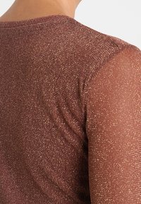 Hnědý svetr s třpytivou texturou, který má kulatý výstřih a krátké, průhledné rukávy. Materiál má lesklý povrch.