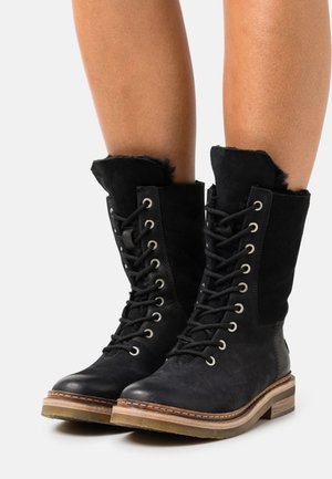 Bottes noires à lacets avec une combinaison de cuir texturé et de daim, présentant un talon en bois bas et un bord supérieur en fourrure.