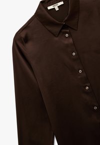 Braunes Satinhemd mit klassischem Kragen, Knopfleiste vorne und langen Ärmeln. Glatte Textur mit kleinen, runden Knöpfen.