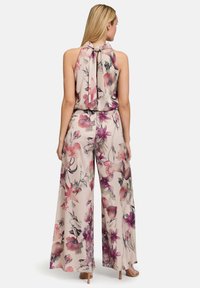 Bloemrijke jumpsuit met een halternek, zachte satijnen stof, lichtroze achtergrond met diep paarse en roze bloemen, wijd uitlopende benen en een gestrikte rugdetail.