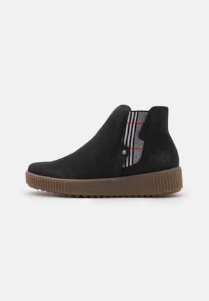 Bottine noire à talon avec semelle en caoutchouc marron, panneau élastique latéral en tartan noir, blanc et rouge, et petit détail de bouton en métal.