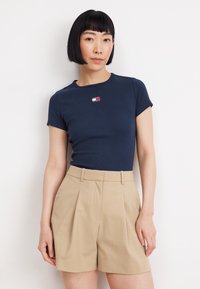 Marinblå ribbad t-shirt med korta ärmar och en liten logotypapplikation. Kombinerad med beige skräddarsydda shorts med veck och sidofickor.