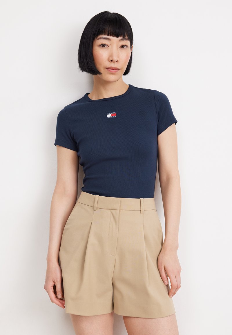 Marinblå ribbad t-shirt med korta ärmar och en liten logotypapplikation. Kombinerad med beige skräddarsydda shorts med veck och sidofickor.