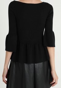 Czarny top peplum wykonany z miękkiego dzianiny, z dekoltem w łódkę i rękawami o długości trzech ćwierci w kształcie dzwonu. Gładka tekstura, dopasowana talia.