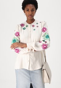 Kremfarget skjorte med fargerik blomsterbrodering i rosa og grønt. Lange puffermer med elastiske mansjetter, kombinert med et denimskjørt.
