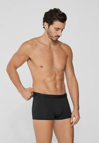 Černé boxerky vyrobené z měkkého materiálu, s přiléhavým střihem a širokým elastickým pasem s logem. Model zkoumá pas.