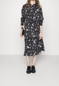 Černé šaty skvěle zdobené fialovými a bílými květy, mají dlouhé rukávy, pásek v pase a rozšířený lem. Spárovány s černými botami.