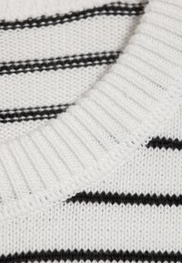 Gros plan d'un tissu tricoté blanc avec de fines rayures horizontales noires et un bord côtelé épais.