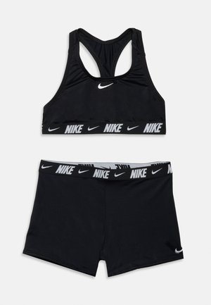 Melns Nike sporta komplekts ar racerback tipa sporta krūšturi un šortiem ar elastīgu jostasvietu, abiem ar baltām Nike logotipiem un swoosh dizainiem.