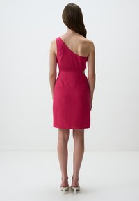 Robe rose ajustée à une épaule en tissu texturé, dotée d'une découpe à la taille et d'un ourlet au genou.