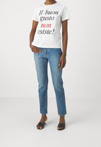 Biała bawełniana koszulka z czarnym i czerwonym napisem, do tego jasnoniebieskie dżinsy i czarne klapki. Prosty, codzienny wygląd.