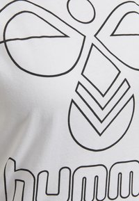Weißes T-Shirt mit auffälligem schwarzem Grafikdesign, das abstrakte Formen und das Wort "humm" in einer runden Schriftart enthält, aus glattem Baumwollstoff.