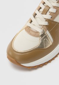Beige en tan sneaker met een bovenwerk van gestructureerde stof, lederen accenten en crèkleurige veters. Voorzien van een rubberen buitenzool met kleine antislipstekels.