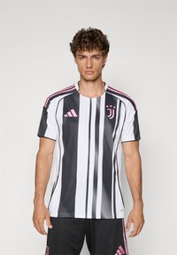 Maillot de football de la Juventus en blanc et noir avec des rayures verticales, présentant des accents roses, des manches courtes et un col rond.
