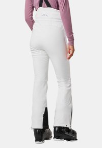 Pantaloni da sci bianchi con bretelle regolabili, vita alta e aperture per le gambe con zip. Styled con dettagli neri e materiale texturizzato.