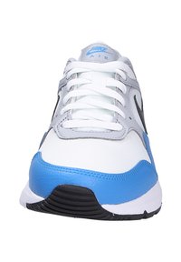 Zapatilla deportiva blanca y gris con acentos azules. Presenta un empeine texturizado, cierre de cordones y una suela negra con tachuelas para mayor agarre.