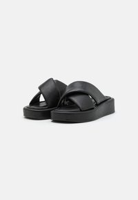 Svart läder sandaler med en tjock plattform och korsade remmar. Slät yta och rundade kanter. Minimalistisk stil.