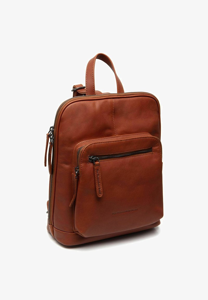 Mochila de cuero marrón con bolsillo con cremallera en el frente, asa superior y textura suave, de pie sobre un fondo blanco.