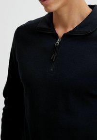 Black half-zip pullover made of textured fabric. Features long sleeves and a classic collar design. Zipper with black pull tab.