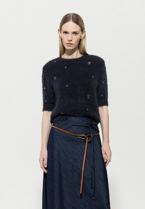 Navy knitted sweater with short sleeves, featuring a fluffy texture and embellishments. Paired with a long denim skirt and a brown belt.