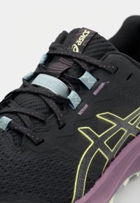 Chaussure de sport noire avec une tige texturée, des accents lavande, des lacets bleu clair et un logo de marque jaune bien visible sur le côté.