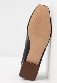 Semelle d'une chaussure en cuir noir avec un talon carré marron, une semelle extérieure côtelée beige, taille 37 et le texte "Made in Spain" visible.