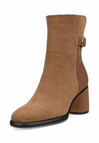 Bottine en daim marron avec une silhouette incurvée, bout carré et un talon épais. Présente une sangle avec un accent de boucle en or.
