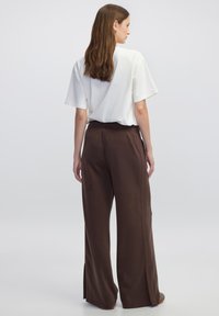 Witte T-shirt met korte mouwen, gecombineerd met bruine wijde broek. De broek heeft zijsplits en een elastische tailleband. Soepele stofstructuur.