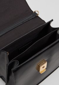 Borsa in pelle nera con chiusura dorata, apertura superiore che mostra due scomparti, uno con una tasca con zip all'interno.