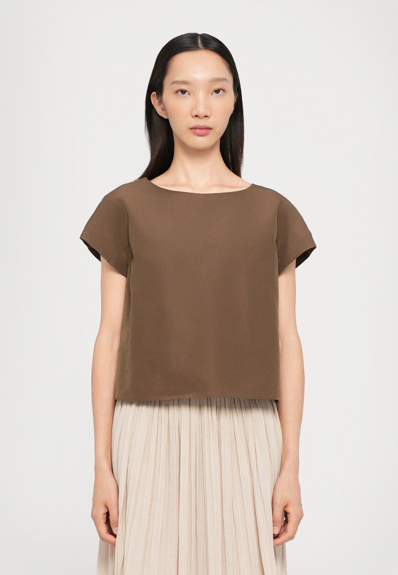 Top brun court avec encolure ronde et manches courtes, en tissu lisse. Associé à une jupe plissée de couleur claire.