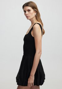 Robe noire avec un haut ajusté et une jupe évasée plissée. Fabriquée en tissu doux avec de larges bretelles et un décolleté arrondi.